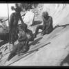 Charlie Murray in foreground with Peter Budge seated behind him and an unidentified man standing. They are shaping tools on a sandstone outcrop near Flynn’s Beach Port Macquarie.